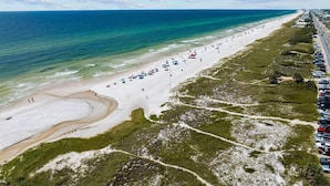 A beach with a road parallel to the shore, lined with parked cars and beach umbrellas.
