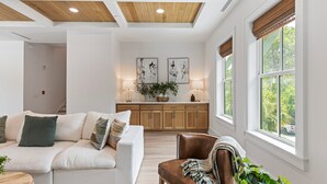 A modern living room with a white sofa, a brown leather chair, and a kitchen in the background.