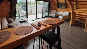 Interior acolhedor de madeira, com uma mesa de jantar comprida, assentos modernos e amplas janelas que oferecem vista para o exterior.