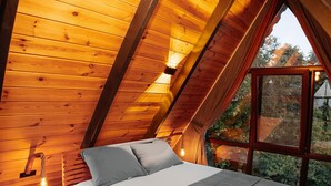 Quarto de madeira aconchegante com cama, almofadas e mesa de cabeceira.