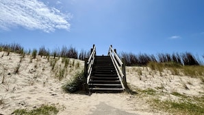 A wooden staircase leading up a sandy dune with a clear sky above.