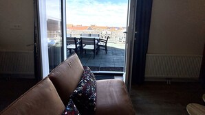 A room with a brown leather sofa, a patterned throw pillow, and a view of an outdoor terrace with tables and chairs.
