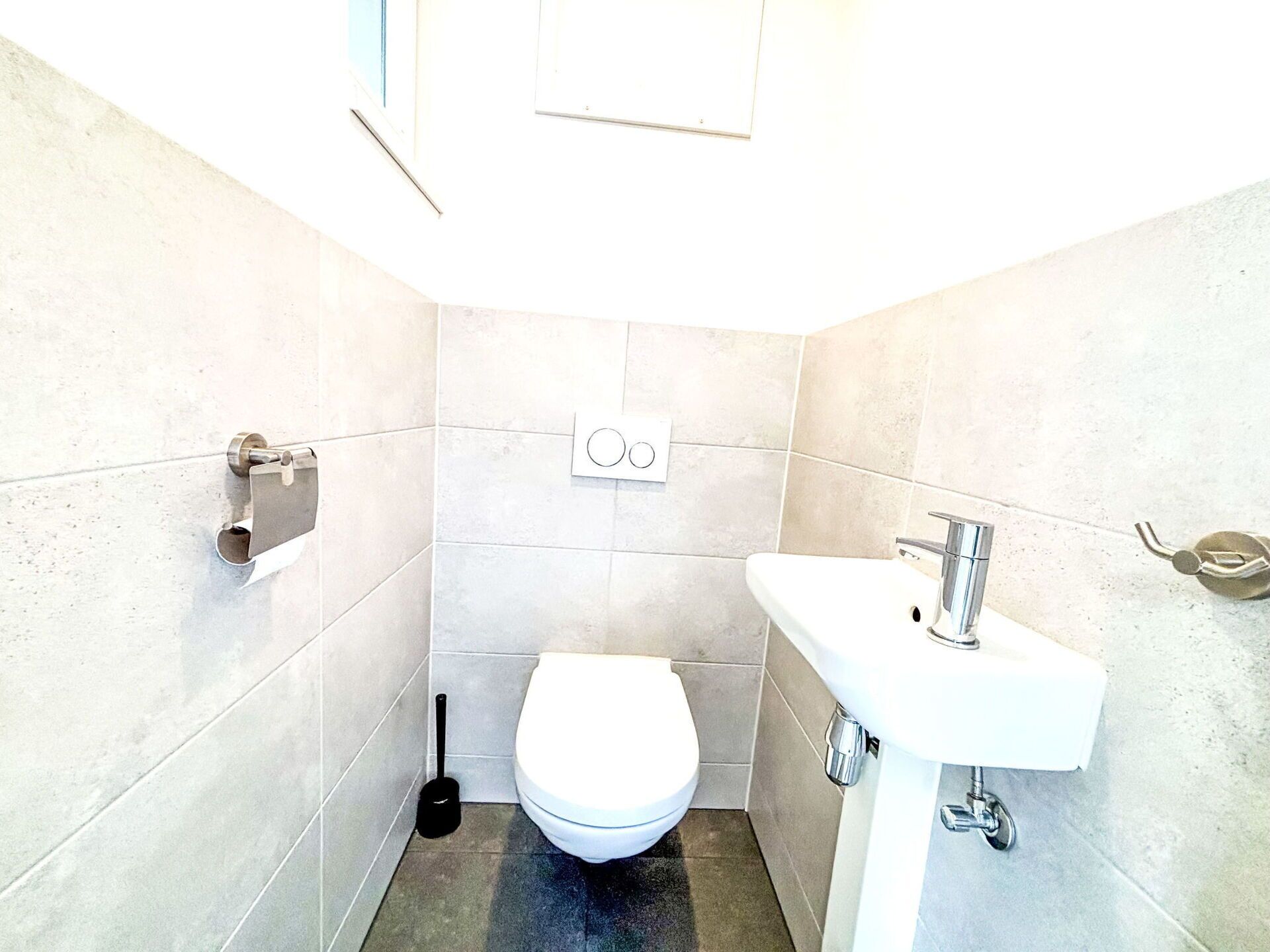 Une petite salle de bain moderne, équipée de toilettes, d’un lavabo et d’un porte-rouleau de papier toilette.