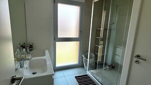 Et moderne badeværelse med vask, spejl og glasvæg omkring brusebadet.