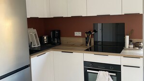 Et moderne køkken med lyse skabe, et rustfrit stål køleskab, en sort komfur og en kaffemaskine.