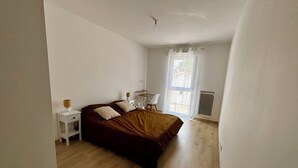 Et soveværelse med seng, natbord, stol og et vindue med gardiner.