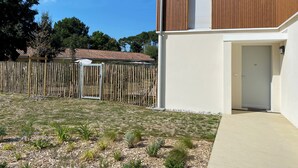 Et moderne hus med træfacade, en hvid dør og en lille have med forskellige planter og et træhegn.