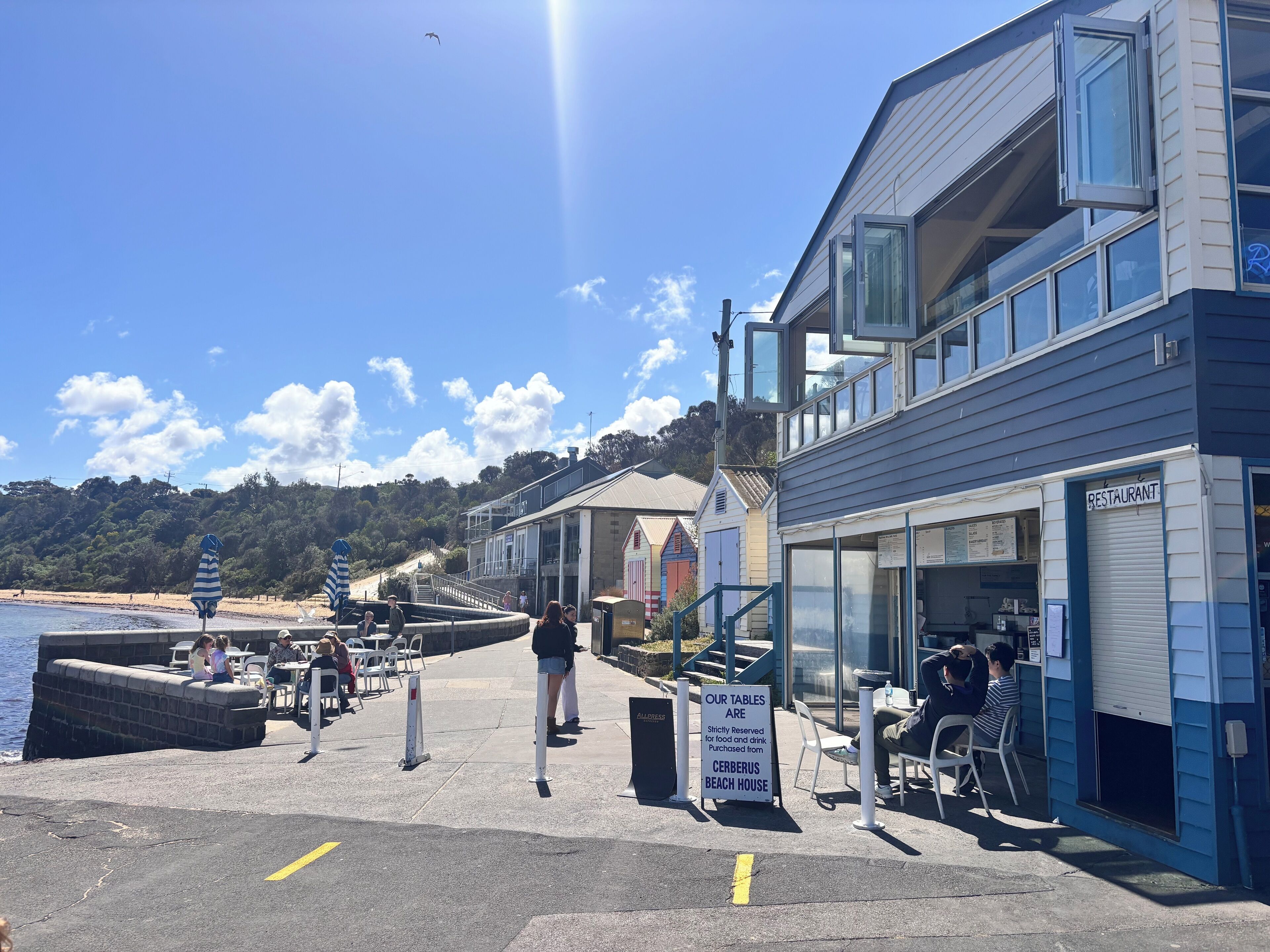 Un restaurante frente al mar con terraza, una playa al fondo y un letrero que indica que las mesas son solo con reserva.