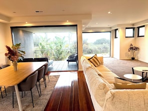 A modern living room with a dining area, a sofa, a small table, and a potted plant. - Melbourne Beachfront Family Home with panoramic view (Black Rock)