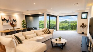 A modern living room with a large sectional sofa, a round coffee table, and a dining area with a table and chairs. - Melbourne Beachfront Family Home with panoramic view (Black Rock)