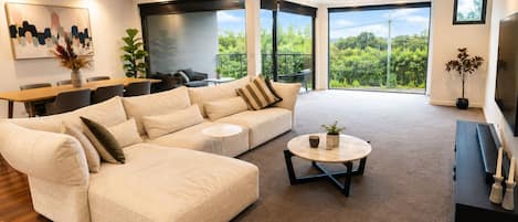 A modern living room with a large sectional sofa, a round coffee table, and a dining area with a table and chairs.