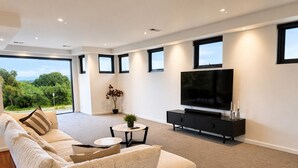 A modern living room with a large sofa, a flat-screen TV, and a small table with a plant. - Melbourne Beachfront Family Home with panoramic view (Black Rock)