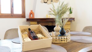 Eine Holzkiste mit einer Flasche und Käse auf einem Tisch, umgeben von gewebten Unterlagen und einer Vase mit Trockenblumen.