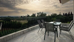 Eine Terrasse mit Tisch und Stühlen, einem Geländer und Blick auf Bäume und eine weite Landschaft.