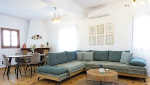 Ein modernes Wohnzimmer mit einer Eckcouch, einem Esstisch mit Stühlen, einem Couchtisch und einer Wand mit gerahmten Kunstwerken.