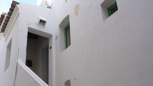 Un edificio blanco con una escalera, un ventanal pequeño y una planta en maceta.