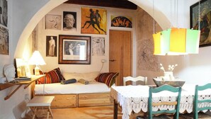 Una habitación acogedora con una cama, una mesa con sillas, una lámpara y varias obras de arte enmarcadas en las paredes.