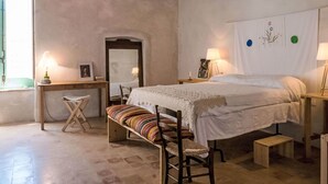 A bedroom with a bed, bedside tables, a desk, a chair, and a small stool.