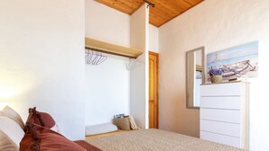 A bedroom with a bed, a wooden ceiling, a wardrobe, and a painting of a boat on the wall.