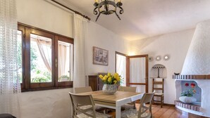 A dining area with a wooden table, two chairs, a vase of flowers, and a fireplace with decorative items.