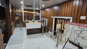 A hotel lobby with marble flooring, wooden paneling, a reception desk, and a distance sign from the hotel. - Hotel kailash parvat (Amb)