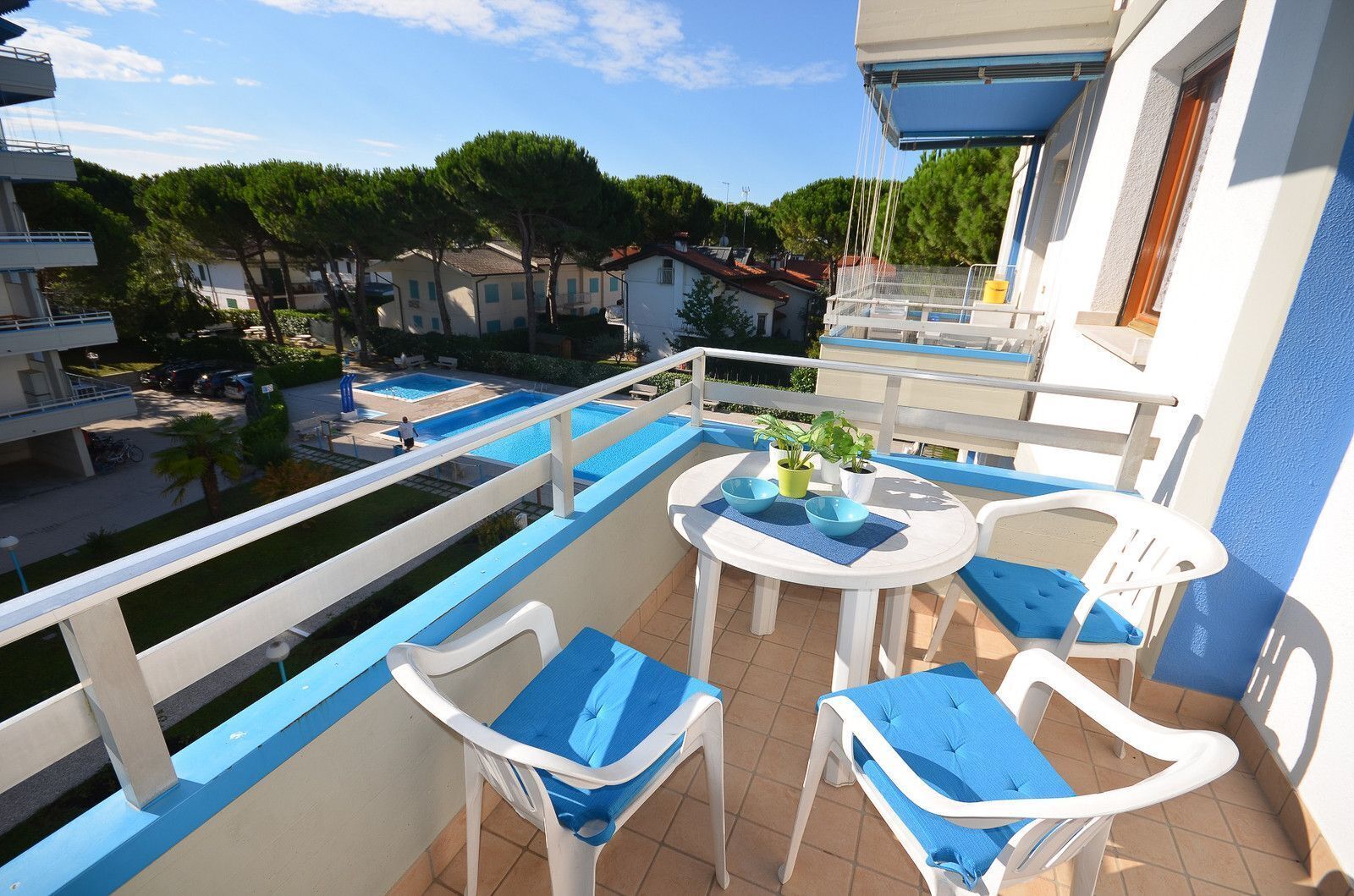 Un balcon avec une piscine, des chaises blanches et une table agrémentée de plantes en pot.