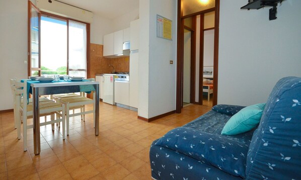 Un espacio habitable compacto con zona de comedor, kitchenette y sofá con cojines estampados.