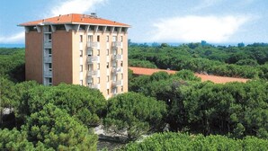 Un edificio de varios pisos con balcones, rodeado de abundante vegetación y un cielo despejado.