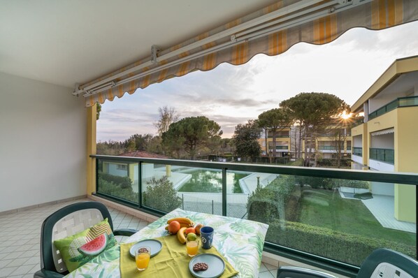 A balcony with a table set for breakfast, overlooking a building and trees.