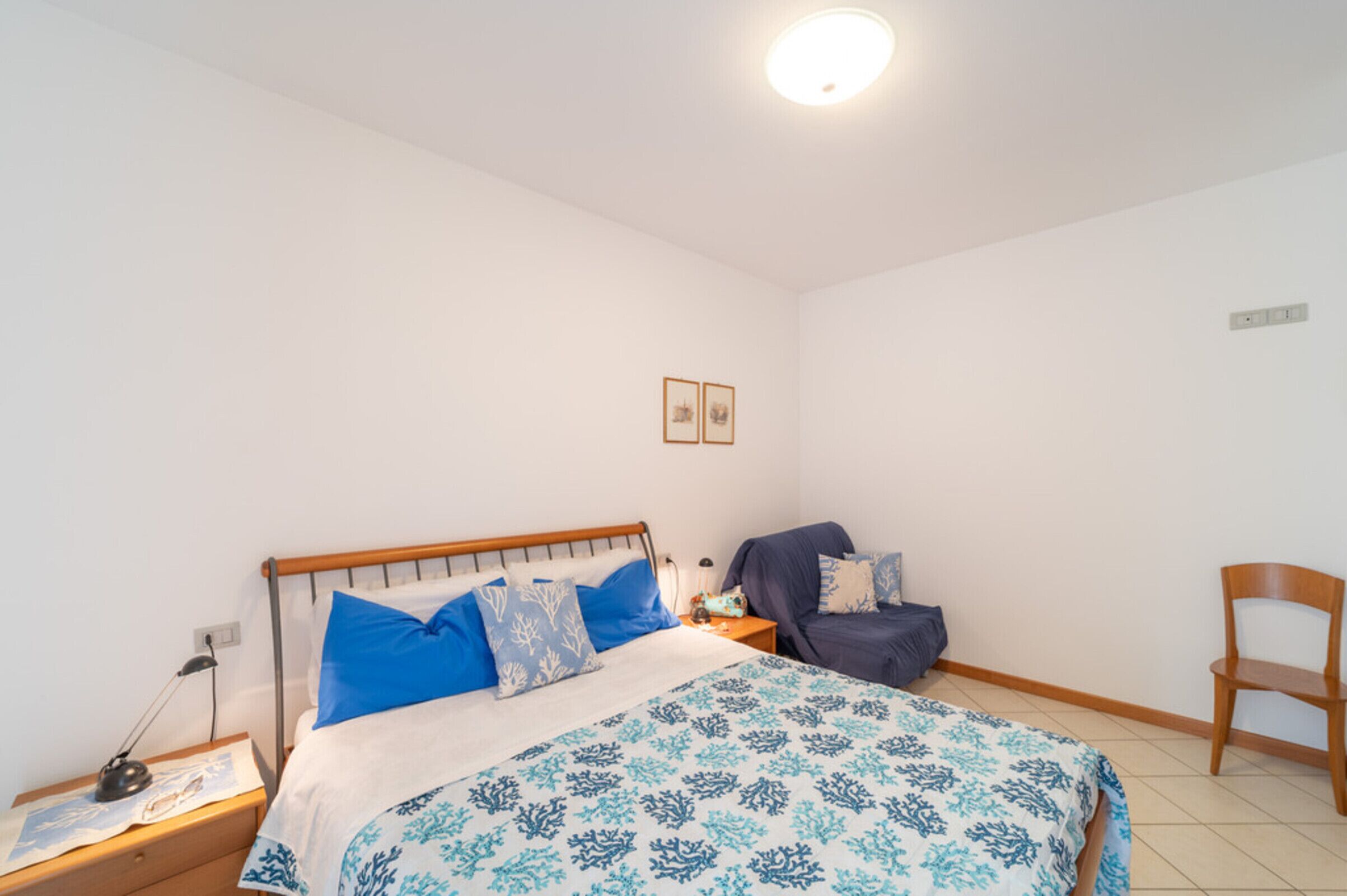Une chambre à coucher comprenant un lit, des tables de chevet, une chaise et un luminaire fixé au mur.