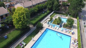Ein Wohngebiet mit einem großen Schwimmbecken, mehreren Liegestühlen und einem gepflegten Rasen.