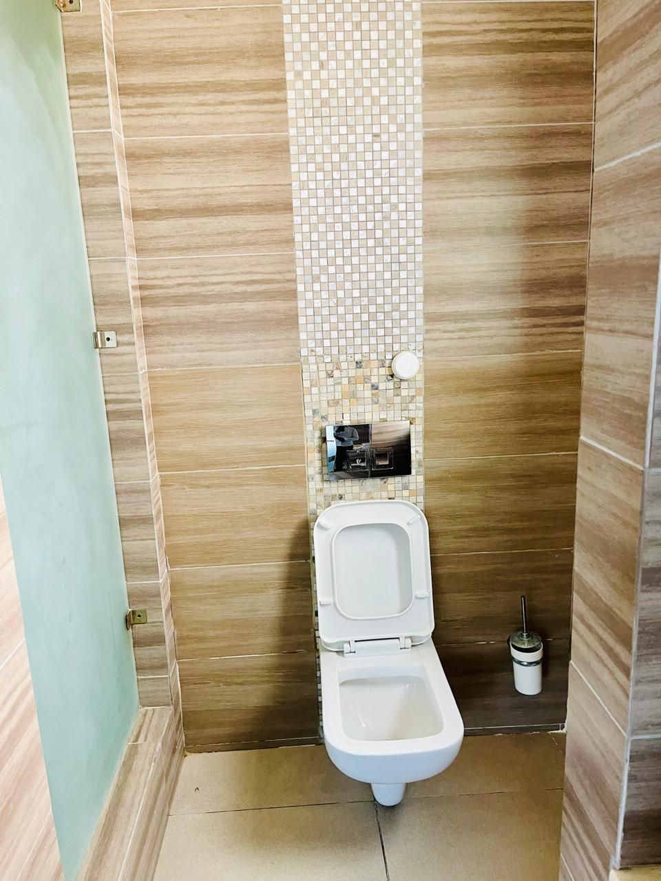 Ein kleines, schmales Badezimmer mit Toilette, einem Wand-Toilettenpapierhalter und einer kleinen Mülltonne.