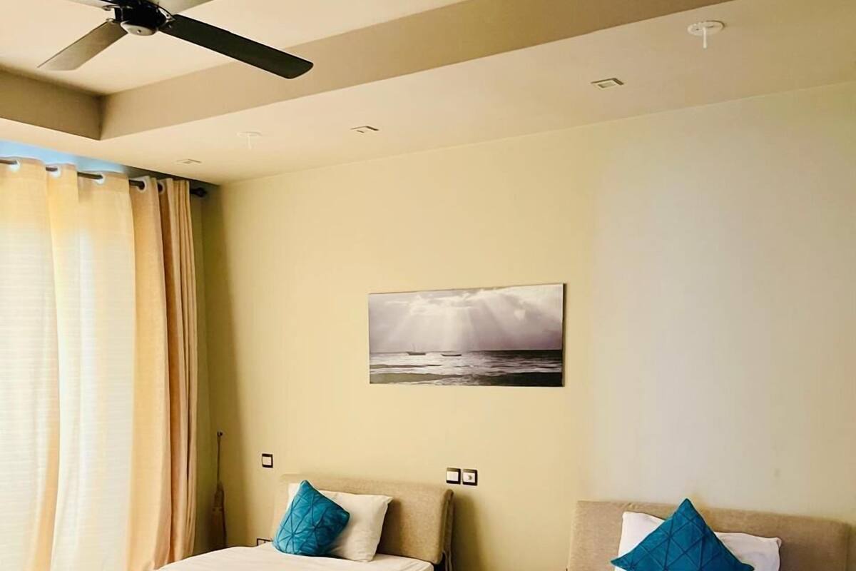 A hotel room with two beds, a ceiling fan, a painting, and a view of the sea.