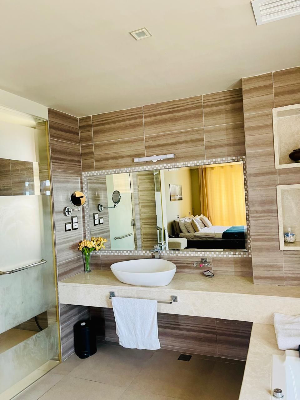 A modern bathroom with a large mirror, a white sink, and a towel rack.