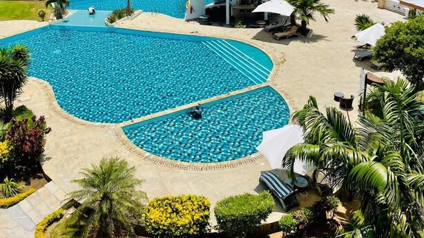 A resort with a large pool, palm trees, and a view of the ocean. - Luxury Oceanline Apartments-Shaza. (Mombasa)
