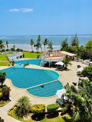 A resort with a large pool, palm trees, and a view of the ocean. - Luxury Oceanline Apartments-Shaza. (Mombasa)