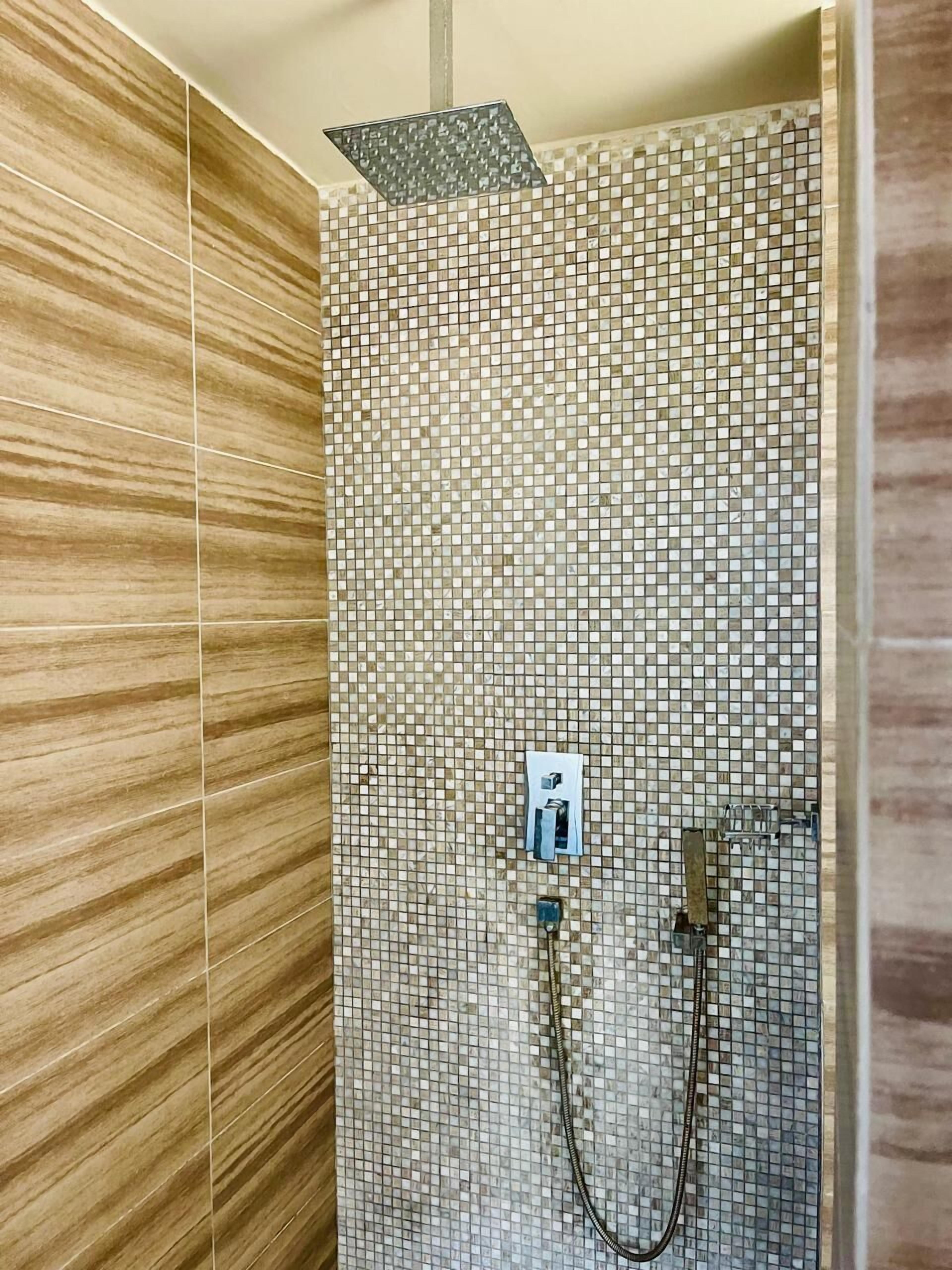 A shower area with a mosaic tile wall and a wooden panel on the left.