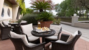Un espace extérieur aménagé avec des chaises en osier et une table, un pot de fleurs et une bouteille de bière.