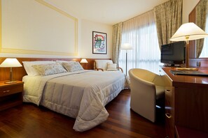 Habitación de hotel con cama, escritorio, silla, televisor y un cuadro en la pared.