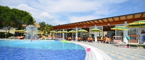 Un espace piscine avec des chaises longues et des parasols, un coin salon abrité et un ciel dégagé.