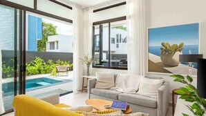 A modern living room with a sofa, a yellow armchair, a coffee table, and a view of a swimming pool and greenery outside.
