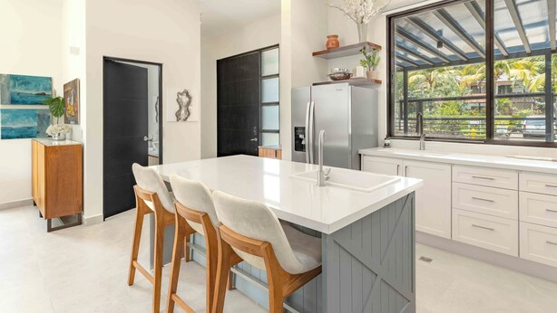 A modern kitchen with a large island, white cabinetry, and a window with a view of greenery.