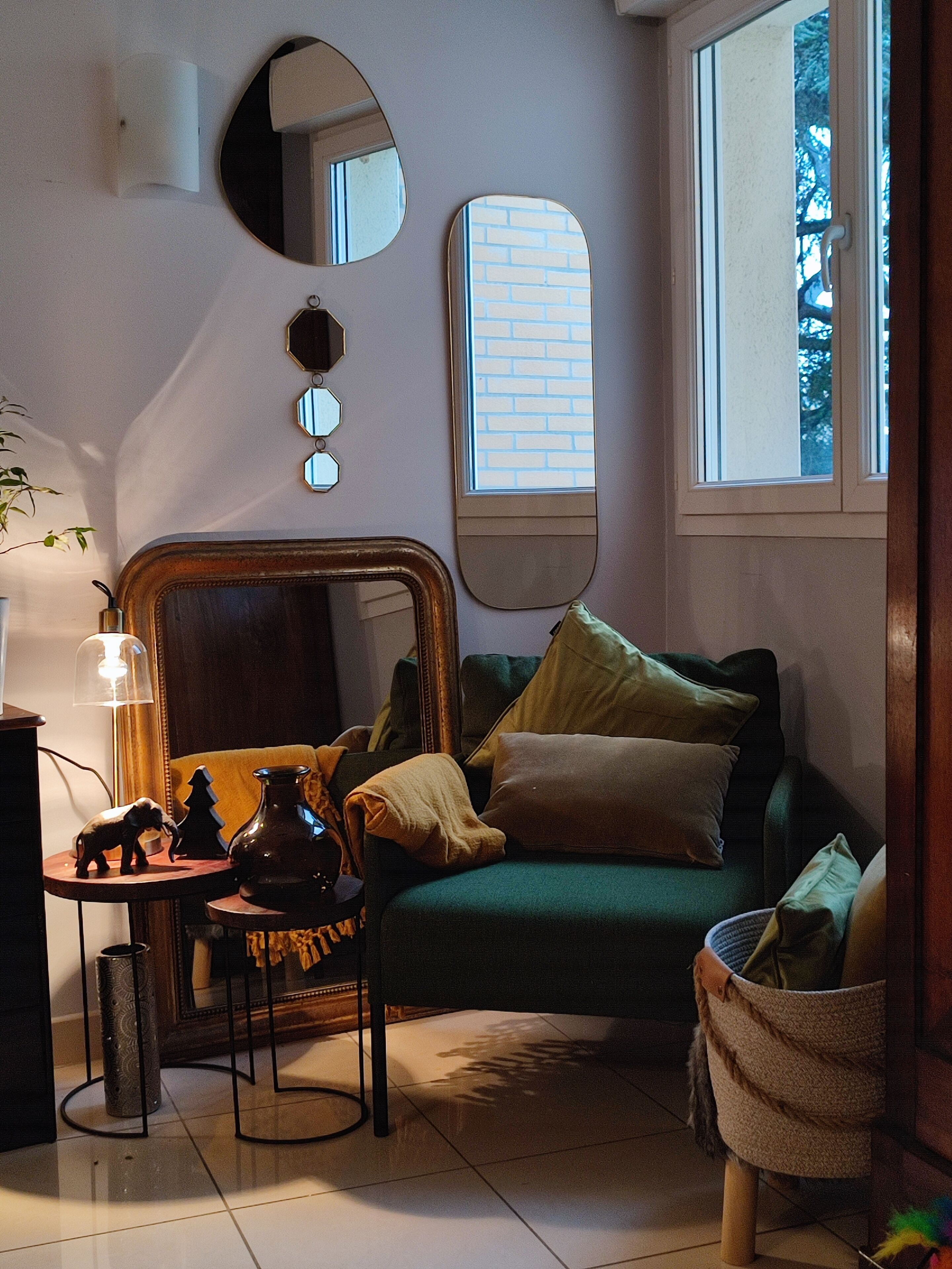 Una sala de estar acogedora con un sofá verde, una mesita con adornos, un espejo y una ventana con vista a árboles.