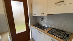 A kitchen with white cabinets, a stainless steel sink, and a gas stove. - Park 17 in Bibione With 2 Bedrooms and 1 Bathrooms (San Michele al Tagliamento)
