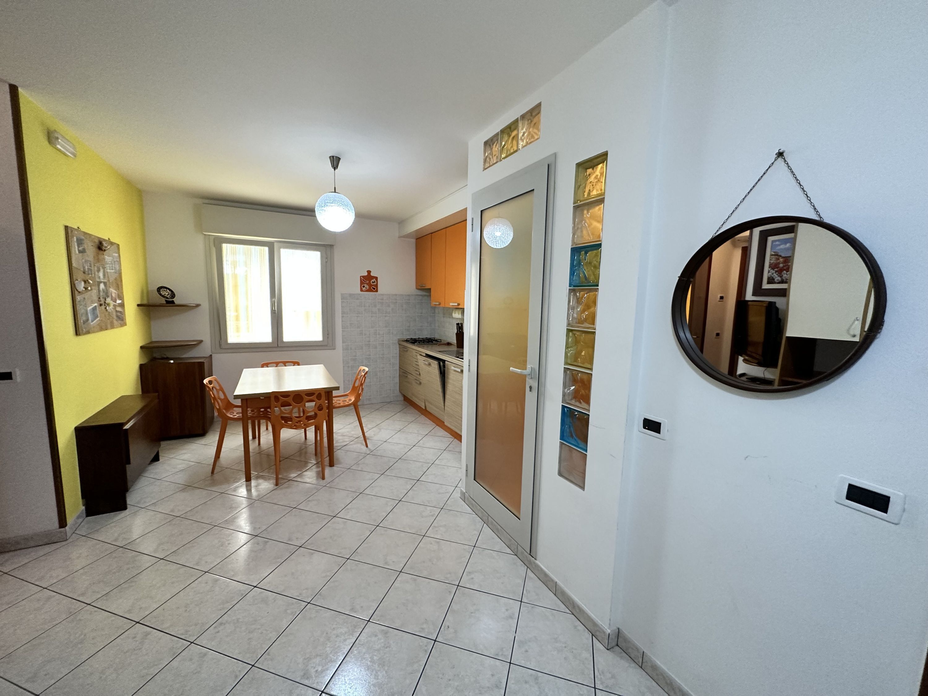 A kitchen with a dining area, a large window, and a mirror on the wall.