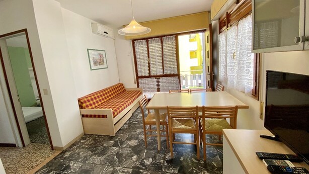 A compact living space with a sofa, dining table, chairs, a TV, and a ceiling light. - Park 15 in Bibione With 2 Bedrooms and 1 Bathrooms (San Michele al Tagliamento)
