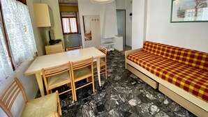 A compact living space with a dining table and chairs, a sofa, a hanging light fixture, and a framed picture on the wall. - Park 15 in Bibione With 2 Bedrooms and 1 Bathrooms (San Michele al Tagliamento)