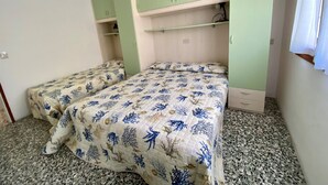 A bedroom with two beds, green cabinets, and a window with white curtains. - Park 15 in Bibione With 2 Bedrooms and 1 Bathrooms (San Michele al Tagliamento)