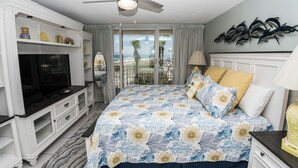 Un dormitorio con una cama grande, televisión y balcón con vista a la playa.