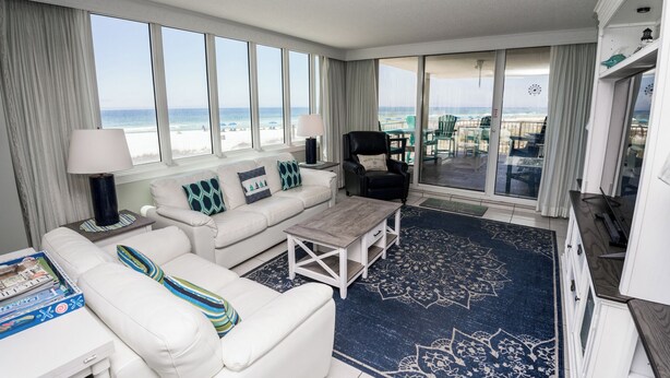 Habitación de hotel con un ventanal grande con vistas a la playa, un sofá blanco, una mesa de centro y vista al océano.
